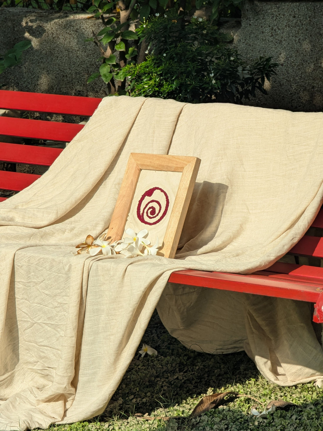 Burrow's logo in a frame, embroidered, sitting on a stretch of linen fabric over a red bench in a park