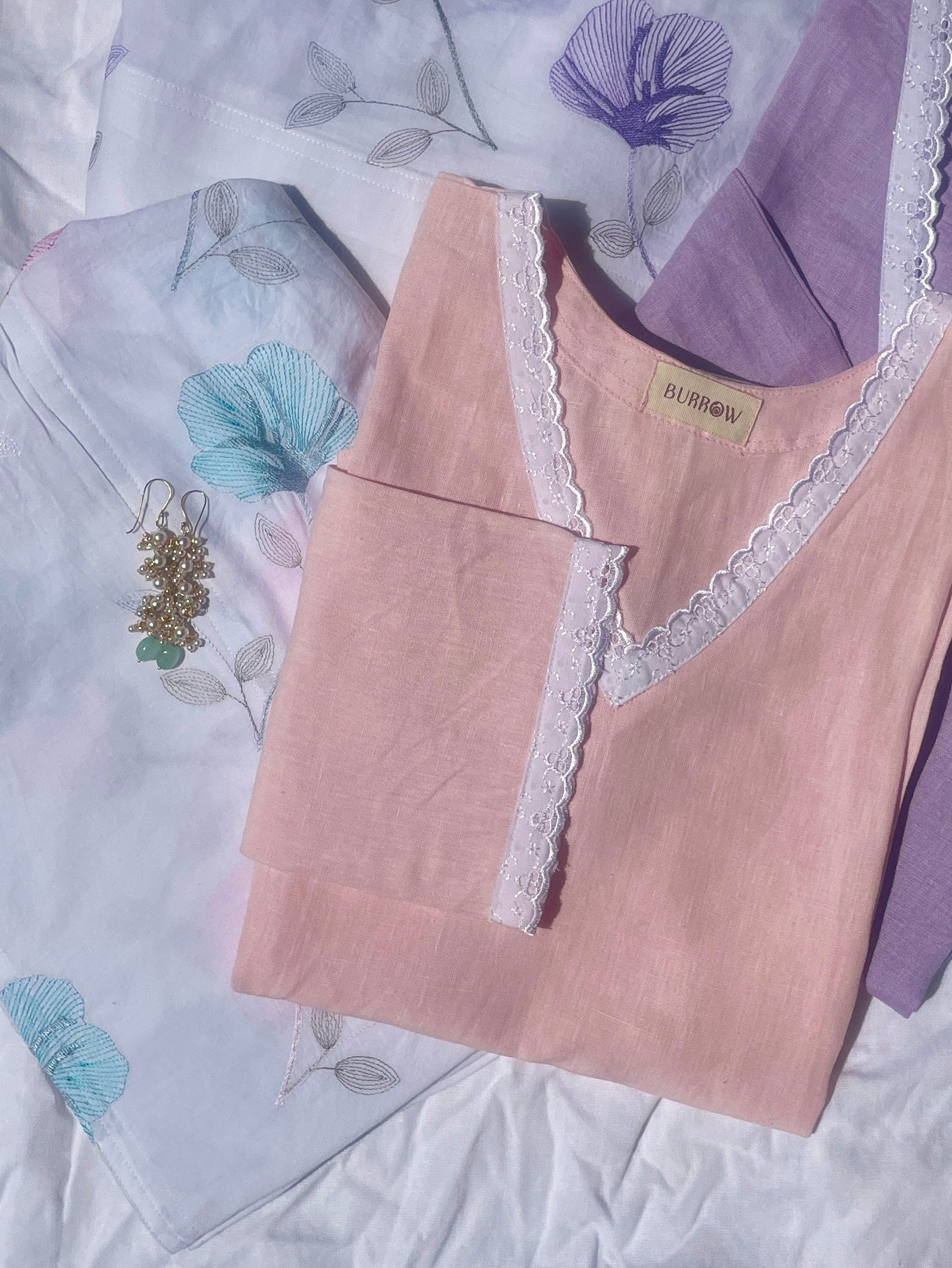 Two lace-trimmed short kurtis, one pink and one purple, on a textured flowery patterned salwar on white background.