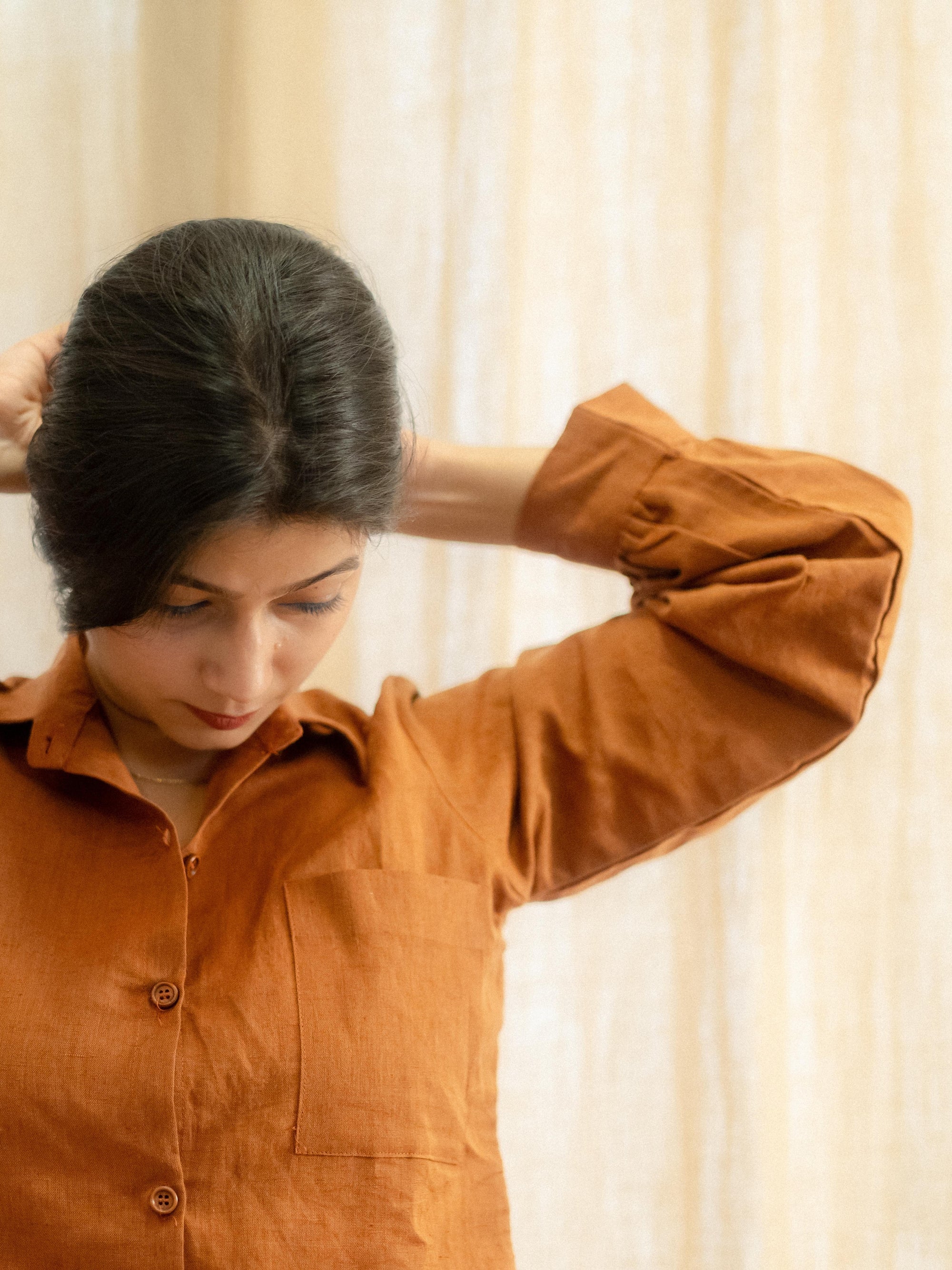 Woman wearing a brown shirt against a beige curtain background